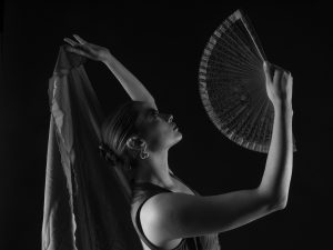 Black and white photo of a flamenco dancer with a fan in a graceful pose, capturing elegance and movement.